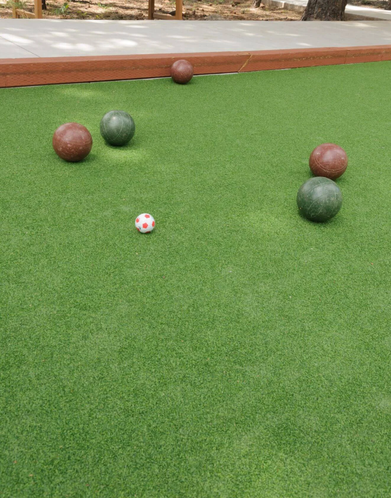 A bocce ball game unfolds on a well-manicured court, featuring San Tan Valley's finest artificial turf installation. Green and brown bocce balls are scattered about, with a small red and white target ball in the center of the lush surface.