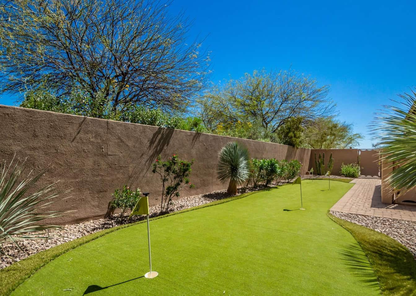 A neatly maintained backyard in San Tan Valley features a small putting green installation surrounded by desert landscaping, including cacti and shrubs. The area is enclosed by a brown stucco wall, with clear blue skies overhead.